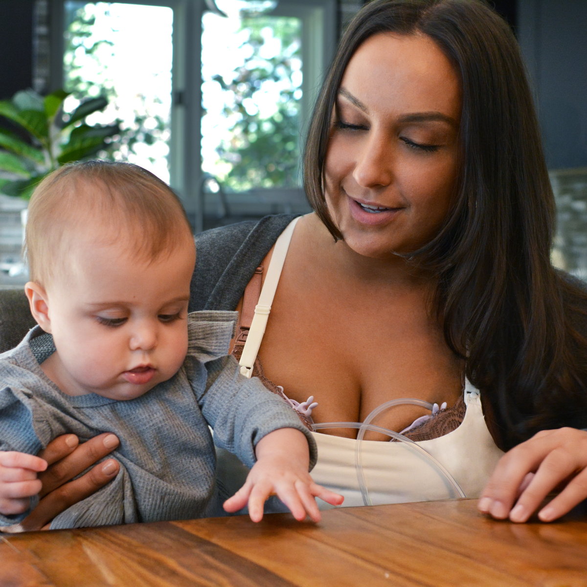 Mom sitting with her baby while wearing Amaris Slim-Cup hands-free breast collection cup